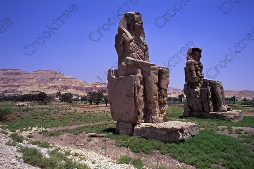 Colossi Memnon EG206424jhp 
 Colossi Memnon statues seated Luxor Theban hills Egypt blue July sunshine that are the most famous remains of Amenhotep's mortuary temple on the northern side of the approach road for the Valley of the Kings, Queens and all the other main West Bank sites. It is the visitors first site of major impact, not far from the main ticket office but is usually visited as a photo opportunity on leaving - recent excavations of the site are finding many hidden buildings and artefacts as well as defining the whole of the remains of the temple complex. 
 Keywords: Egypt, Egyptian, Luxor, West, Bank, Thebes, Theban, hills, fields, River, Nile, landscape, history, archaeology, ancient, Egyptology, Amenhotep, Amenophis, Pharaoh, Tiye, Queen, Mother, mortuary, temple, Colossi, Memnon, seated, statues, side, panels, Union, Upper, Lower, earthquake, damaged, repairs, Severus, blue, sky, sunny, sunshine, roadside, coachstop, excavations, 2000, July, 35mm, Velvia, slides, film, scanned, scan, camera, Nikon, FM2
