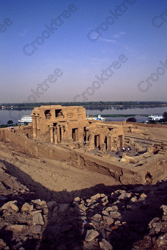 Kom Ombo EG20435jhp 
 Kom Ombo Temple Nile Egypt rare high view Jim Henderson Photo of this beautiful ruined temple just north of Aswan and a regular visit on all Nile Cruises, was principally built by Ptolemy V of Silsilah sandstone. Dedicated to two Gods  Sobek, the crocodile and Horus, the falcon and although it has been damaged over the years, mainly through slipping into the River Nile and some structural damage owing to earthquakes, there are still some wonderful colourful reliefs of the most detailed and delicate style. This trip was special for me in that I got special permission to climb up the back of the temple on the hill behind and match a view I had on a Victorian albumen print; the local Police Chief had to be involved and thanks to a good Kuoni Guide he agreed for me to be accompanied by a policemen as security was still a big thing after the 1997 attacks at Luxor. Unfortunately in the excitement I had forgot to adjust my ASA rating for Velvia and took the photos based on 400ASA-the film maws later pushed to 200asa so there is some increase in grain structure, not a feature of Velvia generally. On this visit some cleaning and restoration was being done to the many painted bas reliefs on the columns-hence the scaffolding and the sun umbrella but the bonus was the reliefs looked particularly vibrant. The time of day also meant some of the museum blocks with deep cut carvings were ideal to photograph as the shadows gave greater emphasis to the excellent cut marks of some iconic hieroglyphic symbols. 
 Keywords: Egypt, East Bank, River Nile, Kom Ombo, Temple, summer, morning, hypostyle hall, pylon, columns, bas, reliefs, restoration, cleaning, conservation, coloured, colored, colours, colors, Silsilah, sandstone, landscape, upright, history, archaeology, ancient, Egyptian, Egyptology, crocodiles, Ptolemaic, Ptolemy, Horus, Haroeris, Harwer, Sobek, Hathor, carvings, detailed, delicate, beautiful, fine, Velvia, slide, film, scans, scan, scanned, 35mm, Nikon, FM, manual, July, 2000